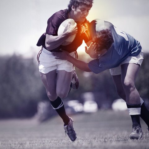 Two rugby players engage in a tackle during a match on a grassy field.