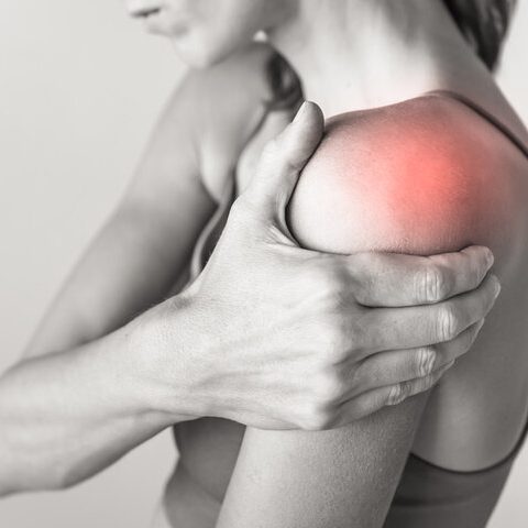 A woman gripping her shoulder, indicating discomfort in the shoulder area.