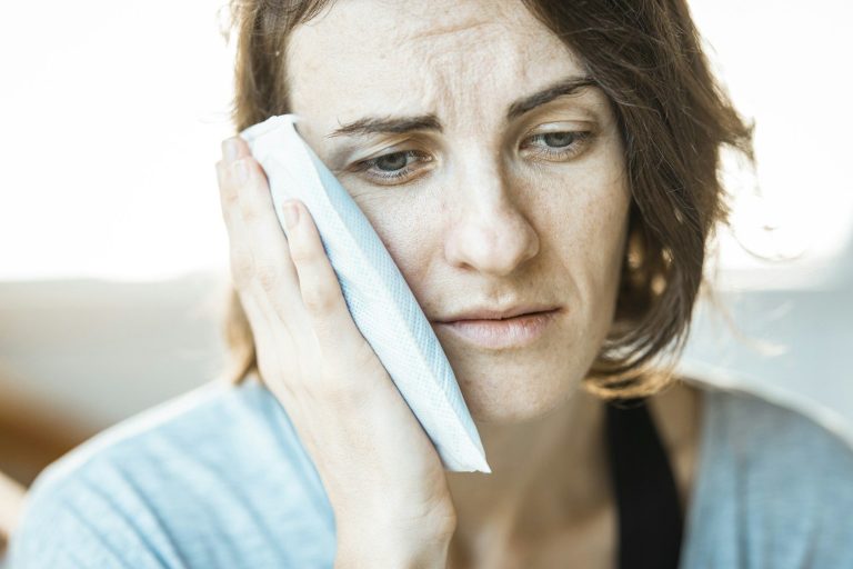 A young woman looks distressed while holding a cool cloth to her face.