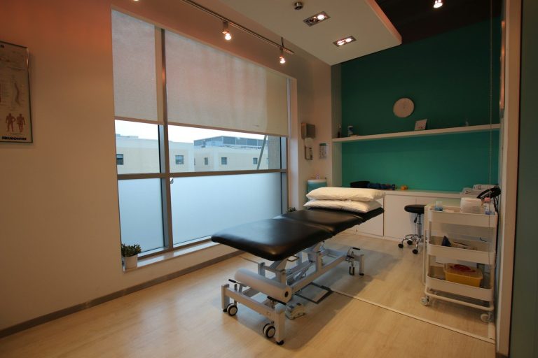 Bright treatment room with a medical examination table and storage cart.